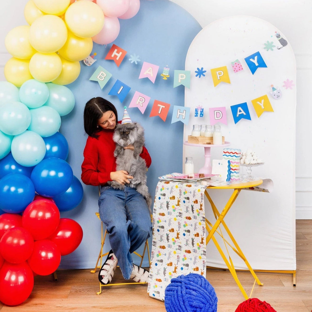 Woman in red sweater posing with cat next to table set with Cat Party Table Runner and banner