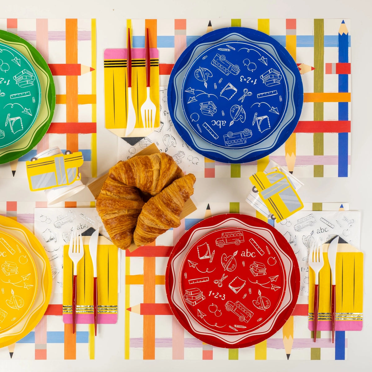 Overhead view of colorful plates in red, blue, green, and yellow set on pencil-stripe placemats for a classroom party.