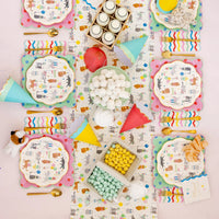 Colorful children's party setup with plates, cups, and decorations on a patterned tablecloth with a cat party theme.