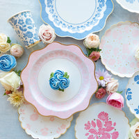 Flat‑lay of Petal Pink Elegant Floral plates surrounded by roses and cupcakes.