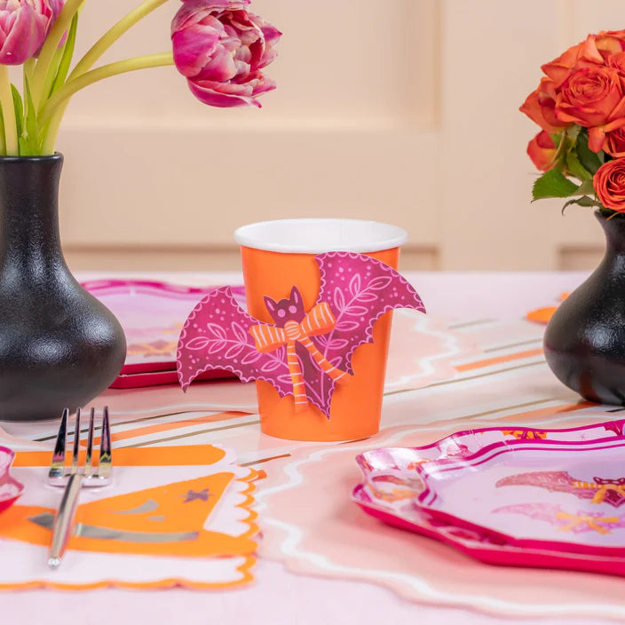 Orange paper cup dressed with a pink bat appliqué on a pastel Halloween tablescape with flowers.