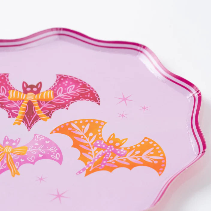 Close up of pink scalloped dinner plate showing pink and orange bats with bows on a lavender background.