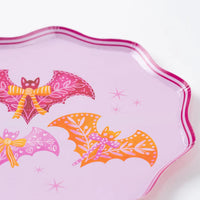 Close up of pink scalloped dinner plate showing pink and orange bats with bows on a lavender background.