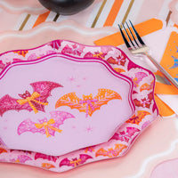 Layered place setting showing pink 10.5 inch bat border plate under a lavender plate on a striped runner.