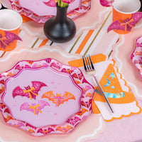 Single place setting with pink bat dinner plate, fork, and orange hat napkin on striped runner.
