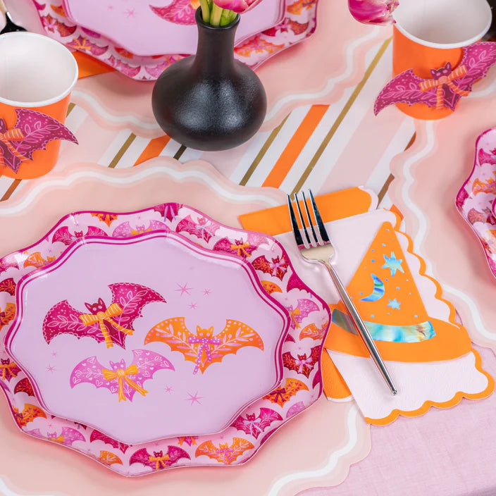Single place setting with pink bat dinner plate, fork, and orange hat napkin on striped runner.