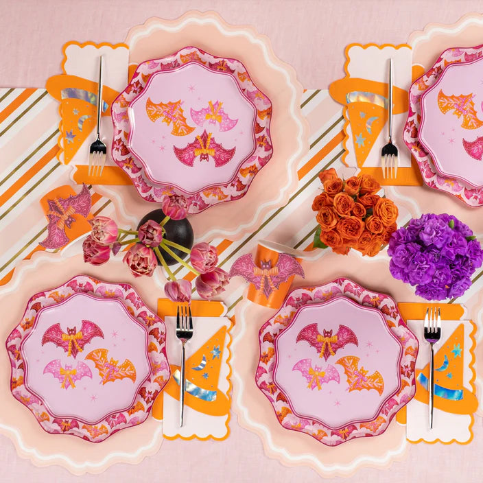 Overhead tablescape with multiple pink bat dinner plates, cups, and florals in orange and purple.