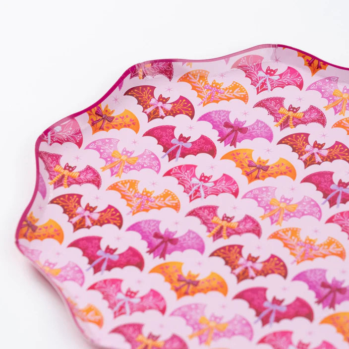 Close up of pink scalloped dinner plate covered in repeating pink and orange bat and bow pattern.