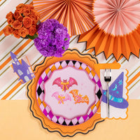 Flat lay place setting with layered plates, party fans, and flowers highlighting the Bats and Bows dinner plate.
