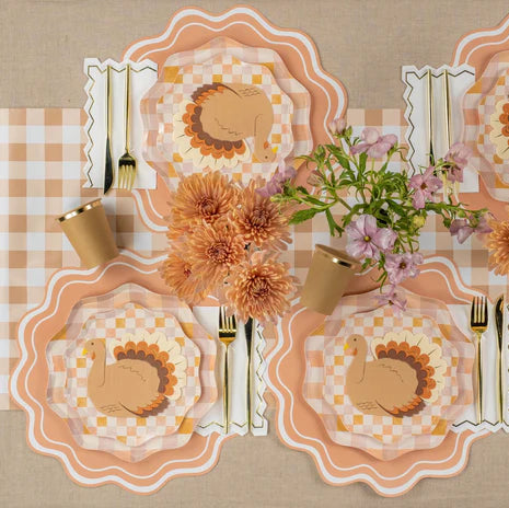 Long harvest table styled on the gingham runner with multiple turkey place settings and florals.