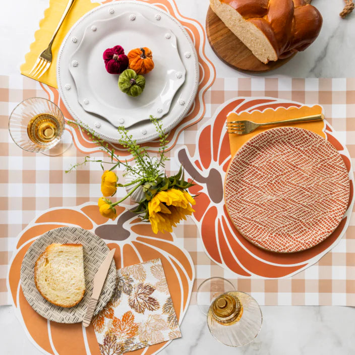 Bread and pumpkin decor on the brown gingham runner with white dinnerware and mustard napkins.