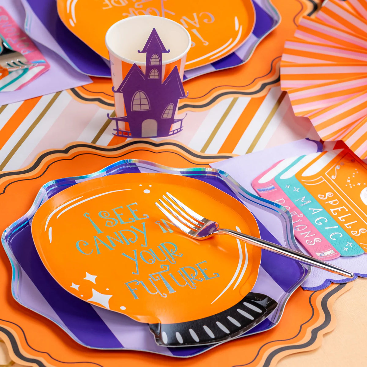 Close styled place setting with crystal ball plate on purple striped plate, fork, and haunted house cup.