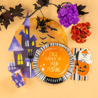 Halloween place setting with crystal ball plate on black and white rim plate beside haunted house placemat and flowers.
