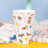 Close view of a single dog party cup on a yellow table showing balloons, confetti, and party dogs.