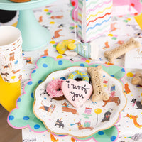 Party table with stacked dog cups beside mint cake stand, scalloped plates, and colorful napkins.
