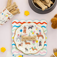 Overhead pup party place setting with dog print plates, bone treats, and a dog party cup filled with biscuits.