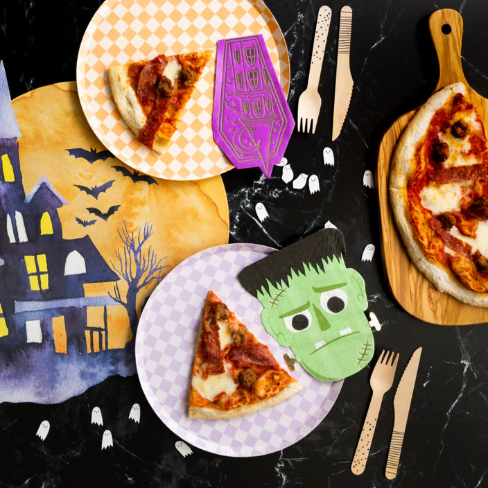 Halloween pizza table flat lay with check plates and a green Frankenstein napkin on black marble.