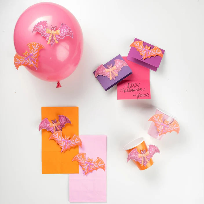 Pink and orange bat and bow accent stickers styled on a pink balloon, favor boxes, napkins, and cups.
