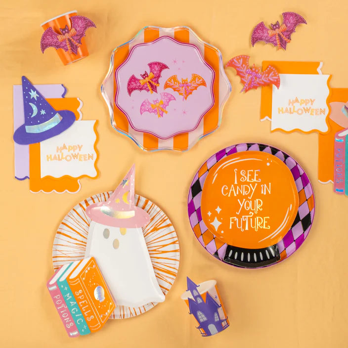 Halloween party flat lay with plates, napkins, and cups accented with pink and orange bat stickers.