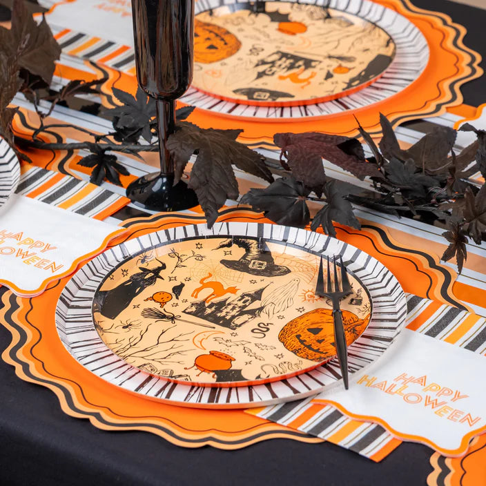 Place setting with Halloween icon dinner plate on striped runner and orange scalloped placemat with black goblet.