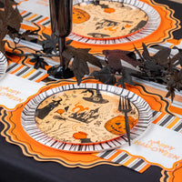 Place setting with Halloween icon dinner plate on striped runner and orange scalloped placemat with black goblet.