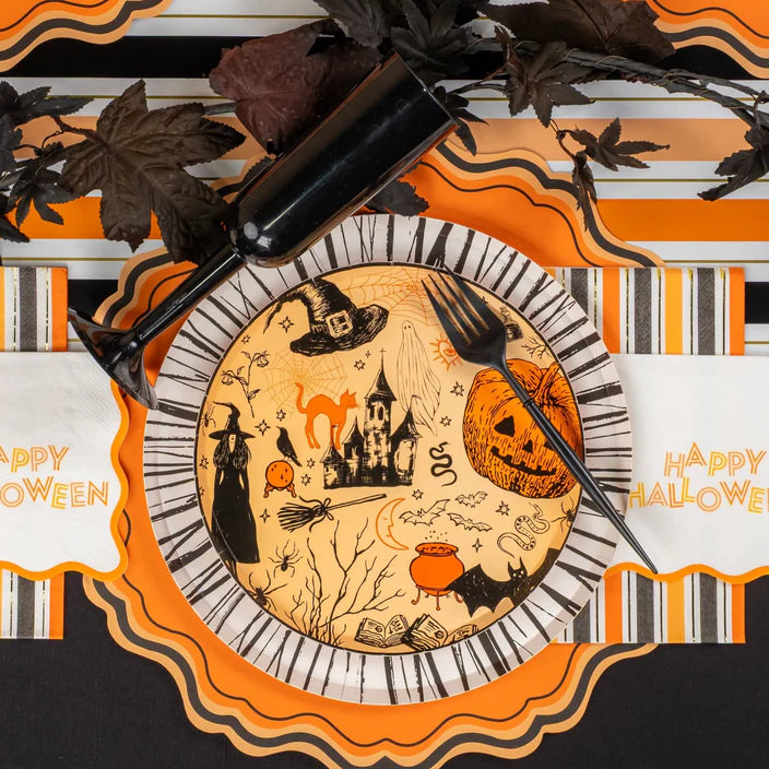 Place setting with icon plate on orange scalloped placemat with black leaves down the center of the table.