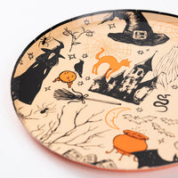 Close up of Halloween icon plate edge showing witch, broom, spiderweb, and castle on a peach orange background.