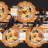 Overhead table showing multiple Halloween icon plates layered on orange scalloped placemats and striped runner.