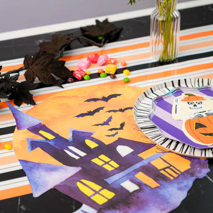 Tablescape with black marble, striped Halloween paper runner, vase of white flowers, candy, and place setting.