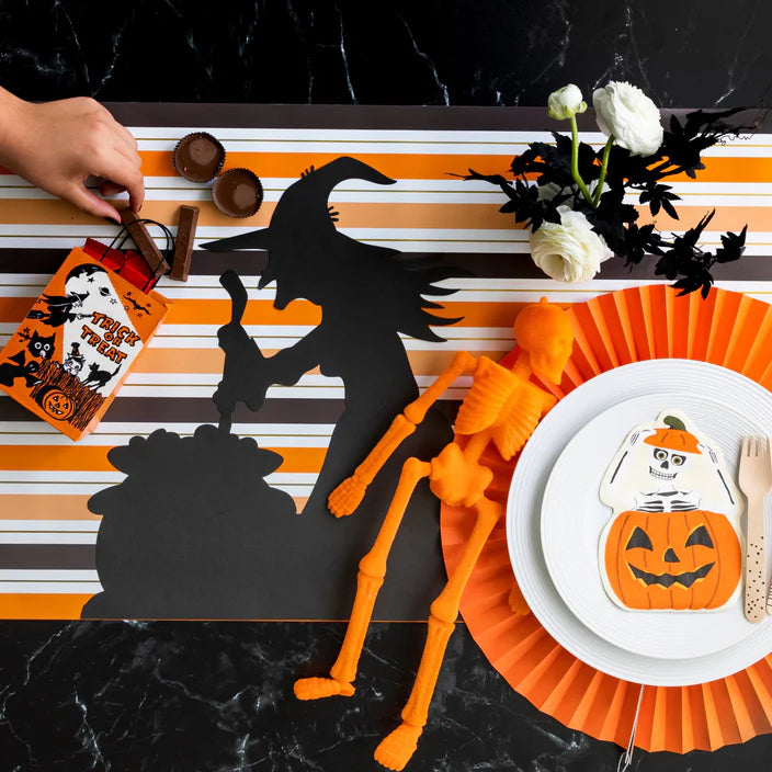 Striped Halloween paper runner styled with black witch silhouette and skeleton accent at a place setting.