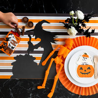 Striped Halloween paper runner styled with black witch silhouette and skeleton accent at a place setting.