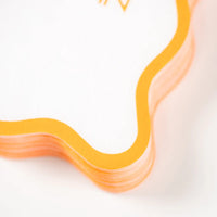 Stack detail of white cocktail napkins with orange scalloped border.