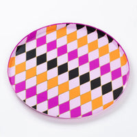 Close up of round dinner plate with pink, purple, orange, and black harlequin diamonds and gold foil lines.