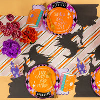 Overhead tablescape with harlequin diamond rim plate layered with an orange plate on a striped runner and witch silhouettes.