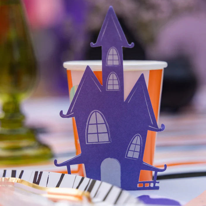 Purple haunted house topper sitting on the rim of an orange striped cup at a party table.