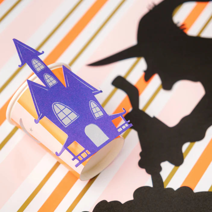 Haunted house cup styled next to witch silhouette on striped table runner.