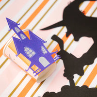 Haunted house cup styled next to witch silhouette on striped table runner.