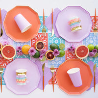 Colorful tablescape with lilac dinner plate layered with citrus and florals, styled with purple paper napkins