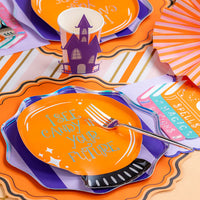 Layered plates with haunted house cup and pastel book stack napkin on a striped runner.