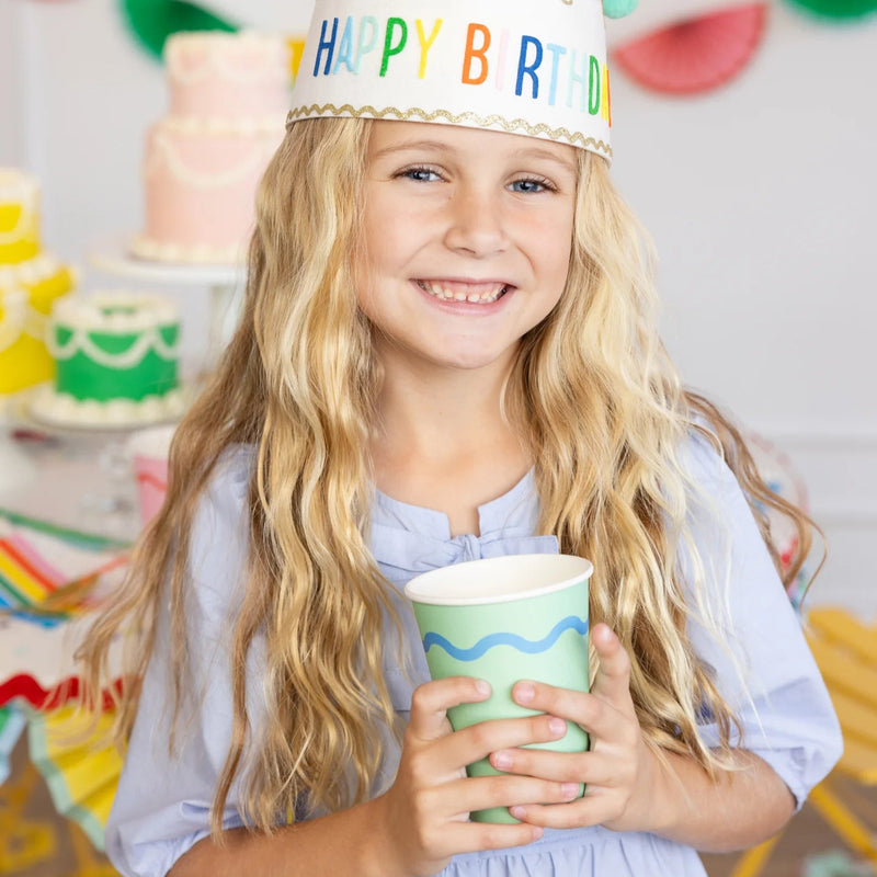 Child holding a mint party cup with blue stripe at a colorful birthday party.