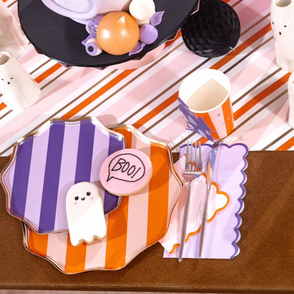 Halloween table closeup with stacked striped plates and lilac scalloped cocktail napkin at the flatware.