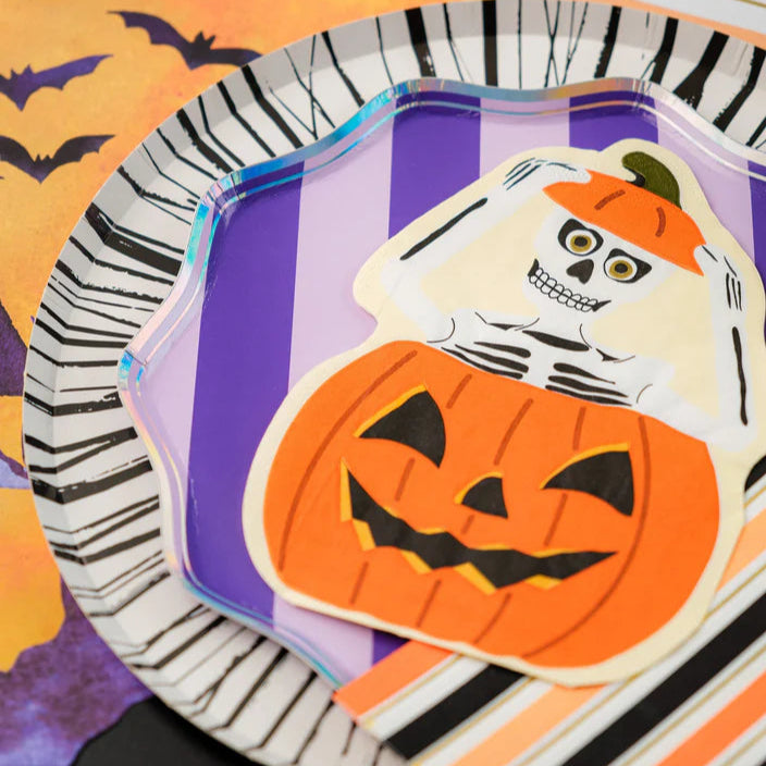 Close view of purple striped plate with skeleton in pumpkin die cut napkin on top.