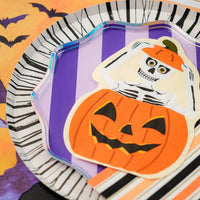 Close view of purple striped plate with skeleton in pumpkin die cut napkin on top.