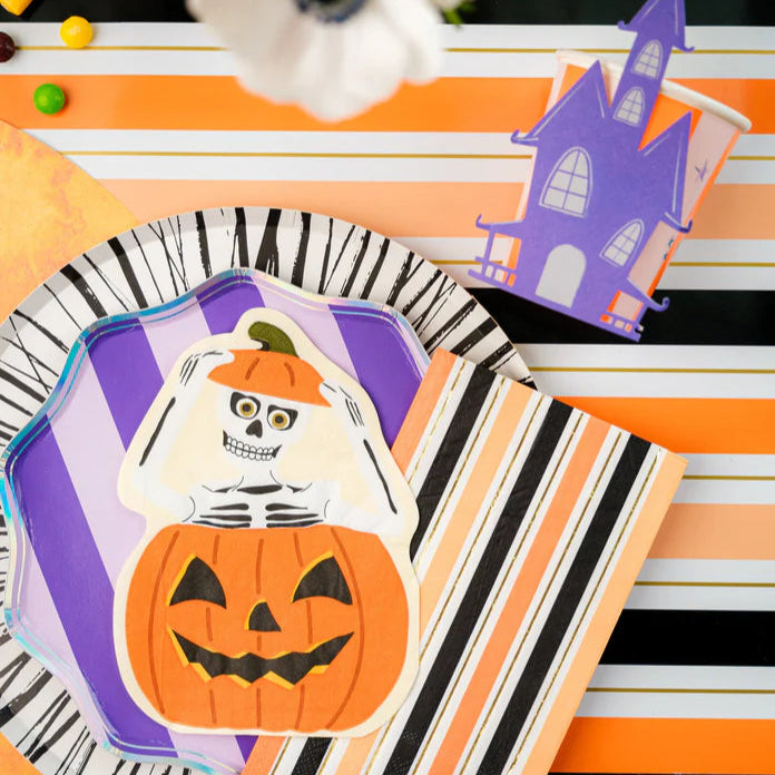 Overhead place setting with striped runner, haunted house cup, and skeleton pumpkin napkin.