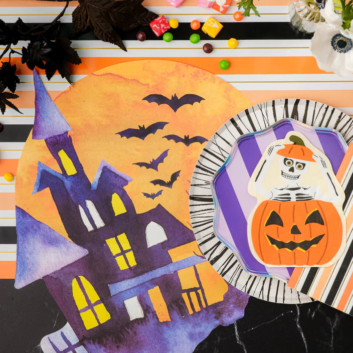 Close overhead of haunted house placemat next to plate topped with skeleton pumpkin napkin.