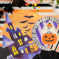 Close overhead of haunted house placemat next to plate topped with skeleton pumpkin napkin.