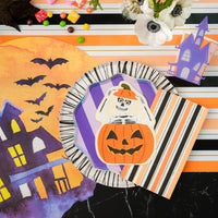 Tablescape with watercolor haunted house placemat and skeleton pumpkin napkin layered over plates.