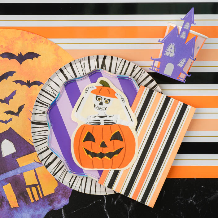 Place setting with purple striped dessert plate layered under a pumpkin skeleton plate and striped napkin.