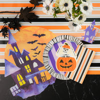 Place setting with purple striped dinner plate layered under pumpkin skeleton plate on a stripe runner.