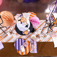 Overhead pastel Halloween table with striped runner and layered purple and orange striped dinner plates.